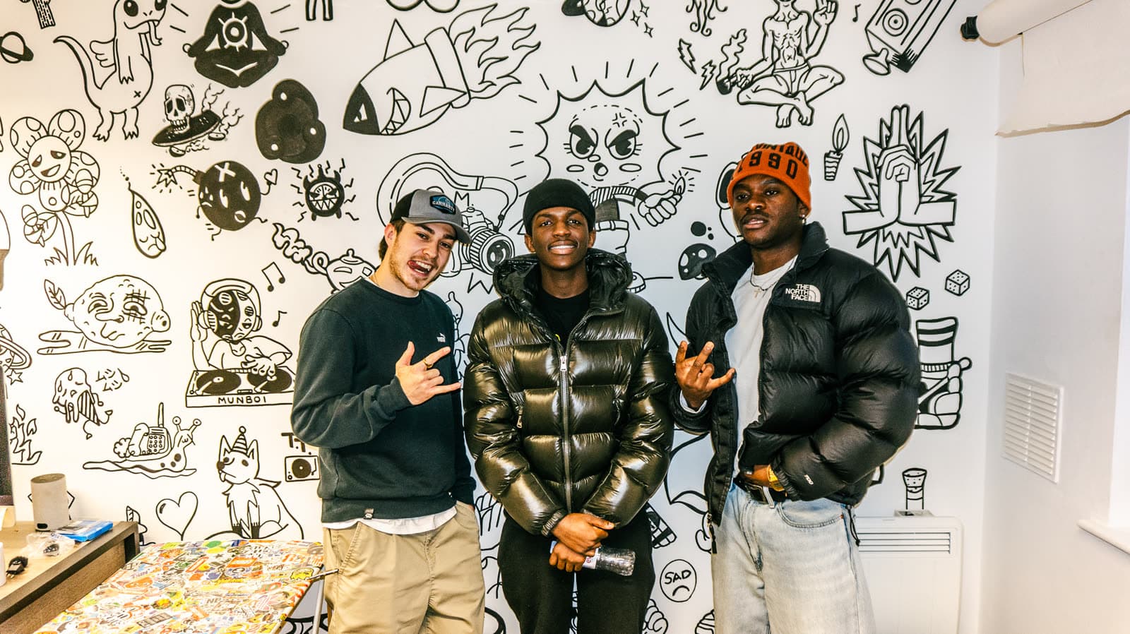 Three young people in front of the studio's illustrated wall mural